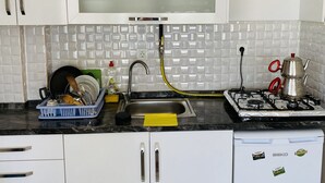 A kitchen with white cabinets, a stainless steel sink, a gas stove, and a dish rack with dishes. - Taner Pansiyon (Edirne)