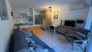 A compact living space with a sofa, a TV, a desk, and a kitchenette. - Beachside Studio - AC, Balcony, Near Shops & Casino, Free WiFi - Perfect Location! (Saint-Raphaël)