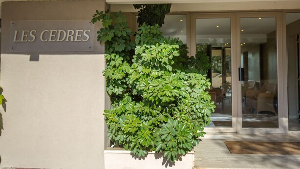 A building entrance with a sign reading "LES CEDRES" and a large planter with green foliage. - Beachside Studio - AC, Balcony, Near Shops & Casino, Free WiFi - Perfect Location! (Saint-Raphaël)