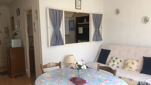 Ein gemütliches Wohnzimmer mit einem runden Tisch, einer blumigen Tischdecke und einer Couch mit gemusterten Kissen.