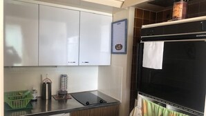 Eine kleine Küche mit weißen Schränken, einem schwarzen Backofen und einem kleinen Kühlschrank.