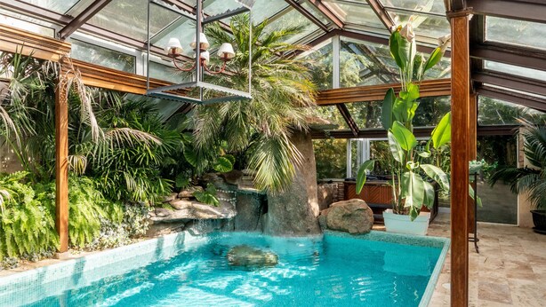 Ein überdachter Innenpool mit tropischer Bepflanzung und Wasserfall.