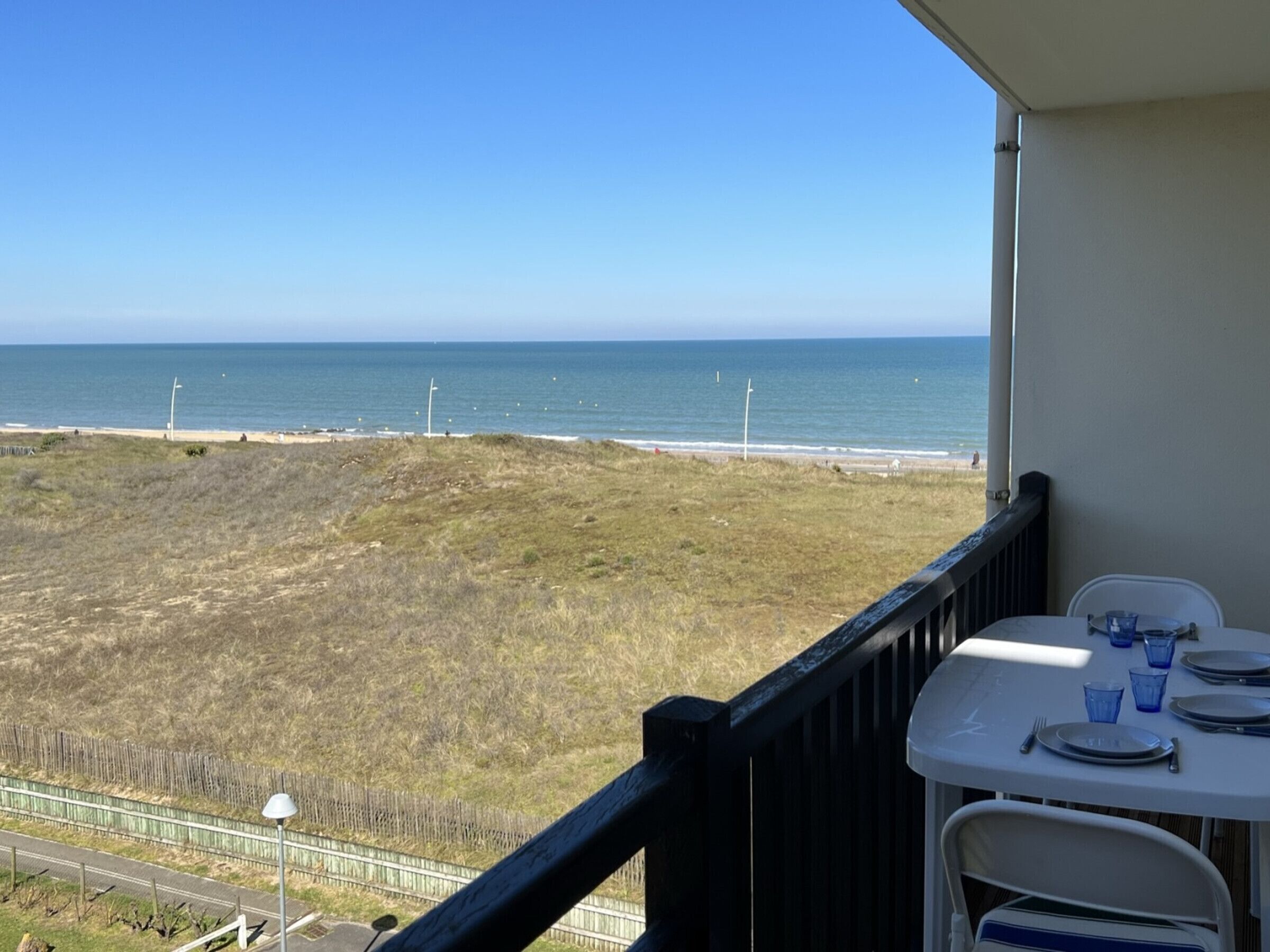 A balcony with a table set for dining, overlooking a beach and the ocean.