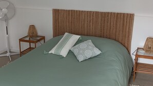 A bedroom with a bed, a woven headboard, a floor lamp, a bedside table, and a wall hanging. - THE HOLIDAYS (Arques)