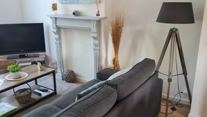 A modern living room with a grey sofa, a flat-screen TV, a fireplace, and a floor lamp. - THE HOLIDAYS (Arques)