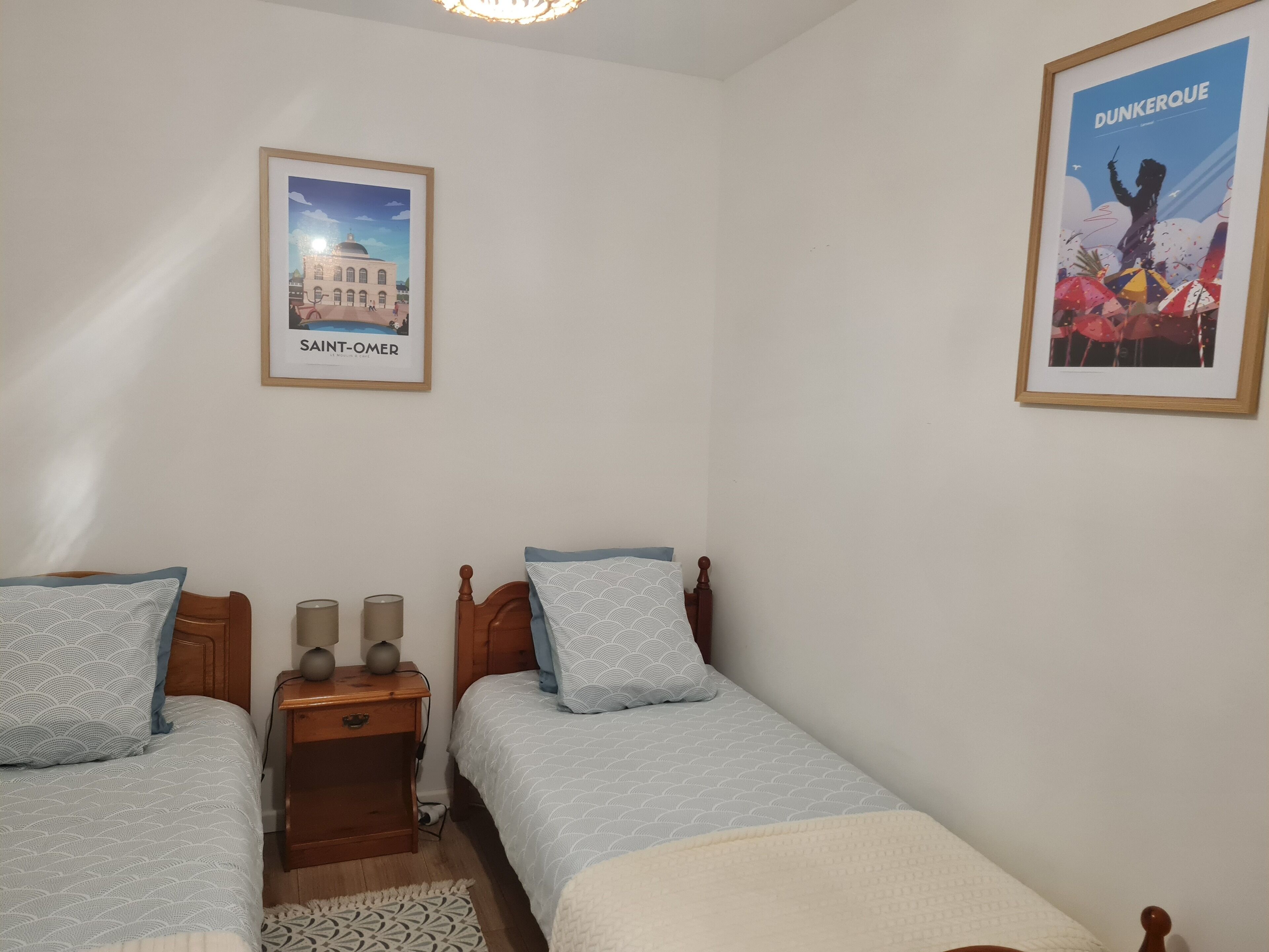 Une chambre avec deux lits, une table de chevet avec des lampes et deux tableaux encadrés au mur.