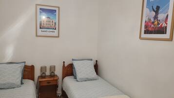 Une chambre avec deux lits, une table de chevet avec des lampes et deux tableaux encadrés au mur.
