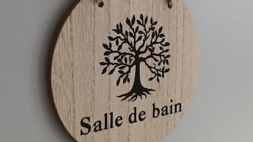 Een rond houten bord met een boom en de tekst 'Salle de bain' aan een muur bevestigd.