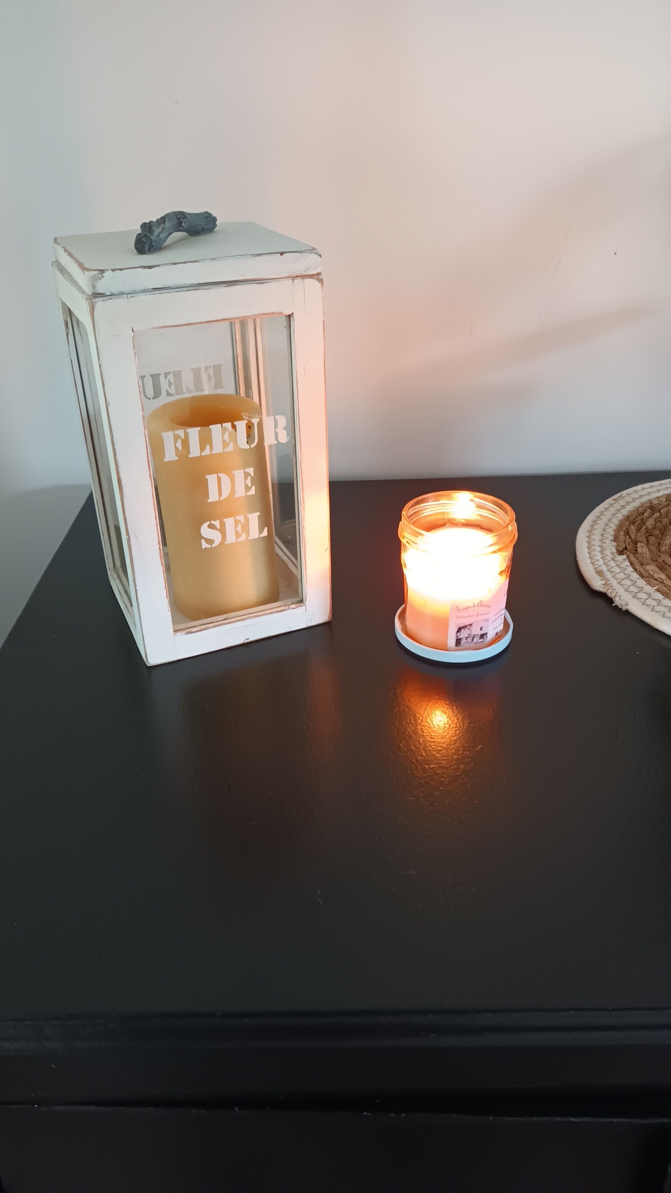 Una vela en un tarro de cristal sobre una mesa negra, junto a una caja blanca con texto.