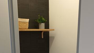 Une petite salle de bain avec des toilettes, une étagère avec une plante et un panier.