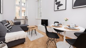 Un salon moderne avec un canapé gris, une table basse blanche, des chaises noires et un téléviseur posé sur un meuble blanc.