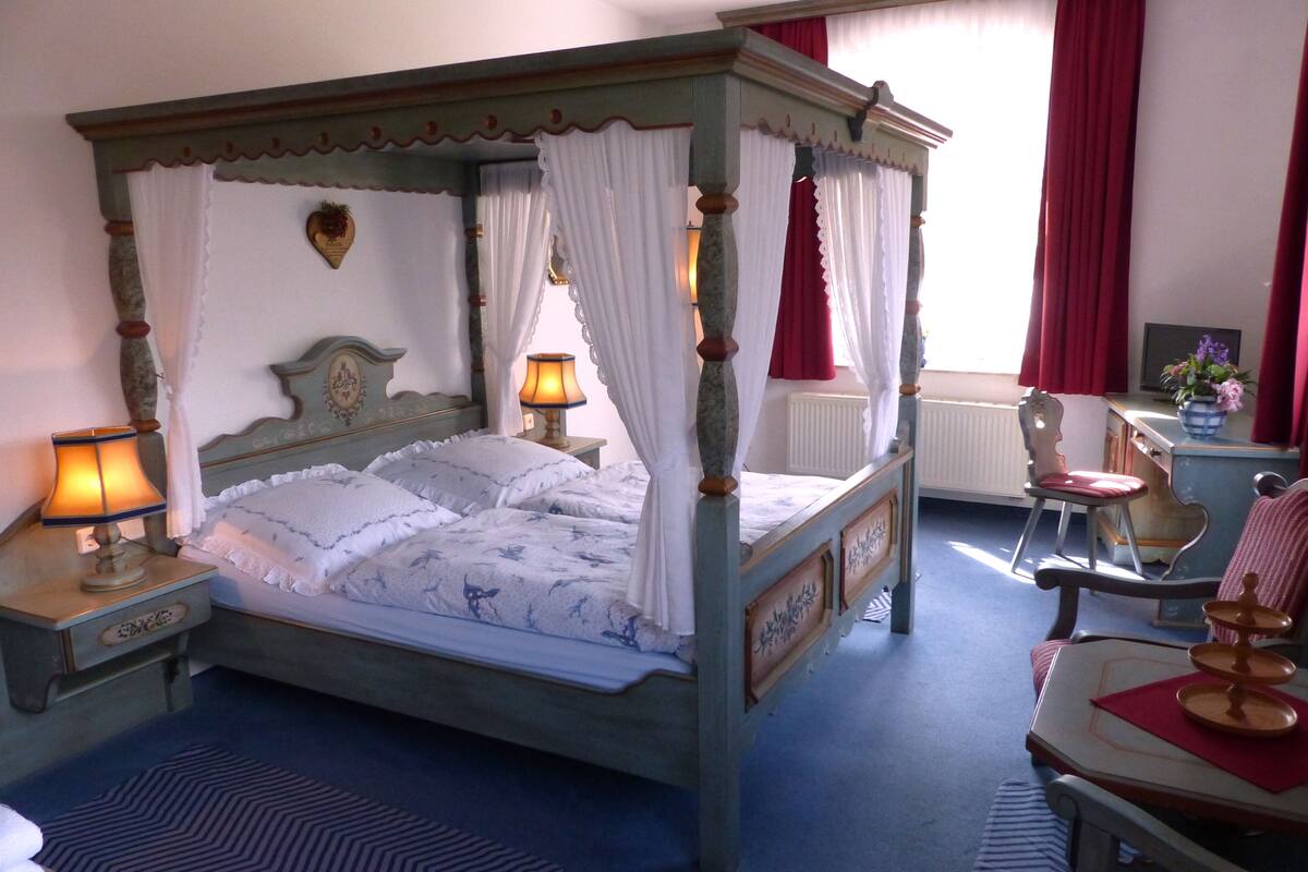 A four-poster bed with a canopy, a bedside table with a lamp, a chair, and a small table with a tray.