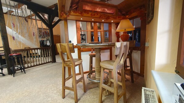 Un comedor acogedor con sillas de madera y una mesa, una escalera con barandilla, y una pared decorativa con elementos colgantes.