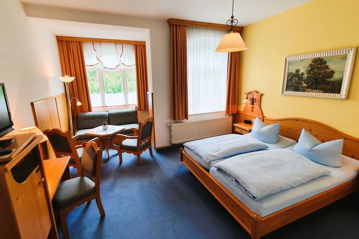 A hotel room with a bed, a desk with a chair, a television, and a painting on the wall.