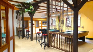 A billiards room with a pool table, bar stools, and a wooden partition with hanging decorations. - Hotel Seiffener Hof (Seiffen)