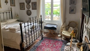 Een klassieke slaapkamer met een bed, een stoel, een radiator en een raam met gordijnen.