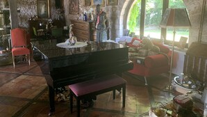 Een ruime woonkamer met een vleugelpiano, een rode bank en een stenen muur.