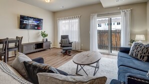 Una sala de estar con televisor de pantalla plana, una mesa de comedor, un sofá y un balcón con vistas a una zona residencial.