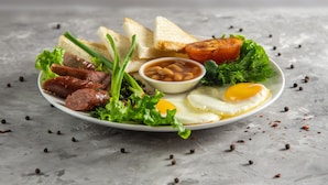 A plate of breakfast food including sausages, eggs, toast, and a small bowl of beans. - Hotel Touristan Bishkek (Bishkek)