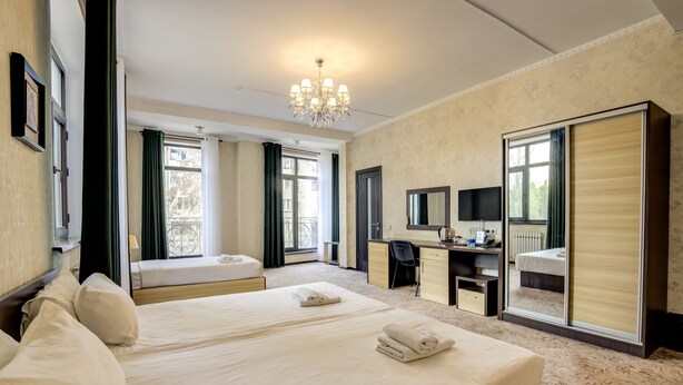A hotel room with two beds, a desk, a chair, a television, and a large mirror. - Hotel Touristan Bishkek (Bishkek)