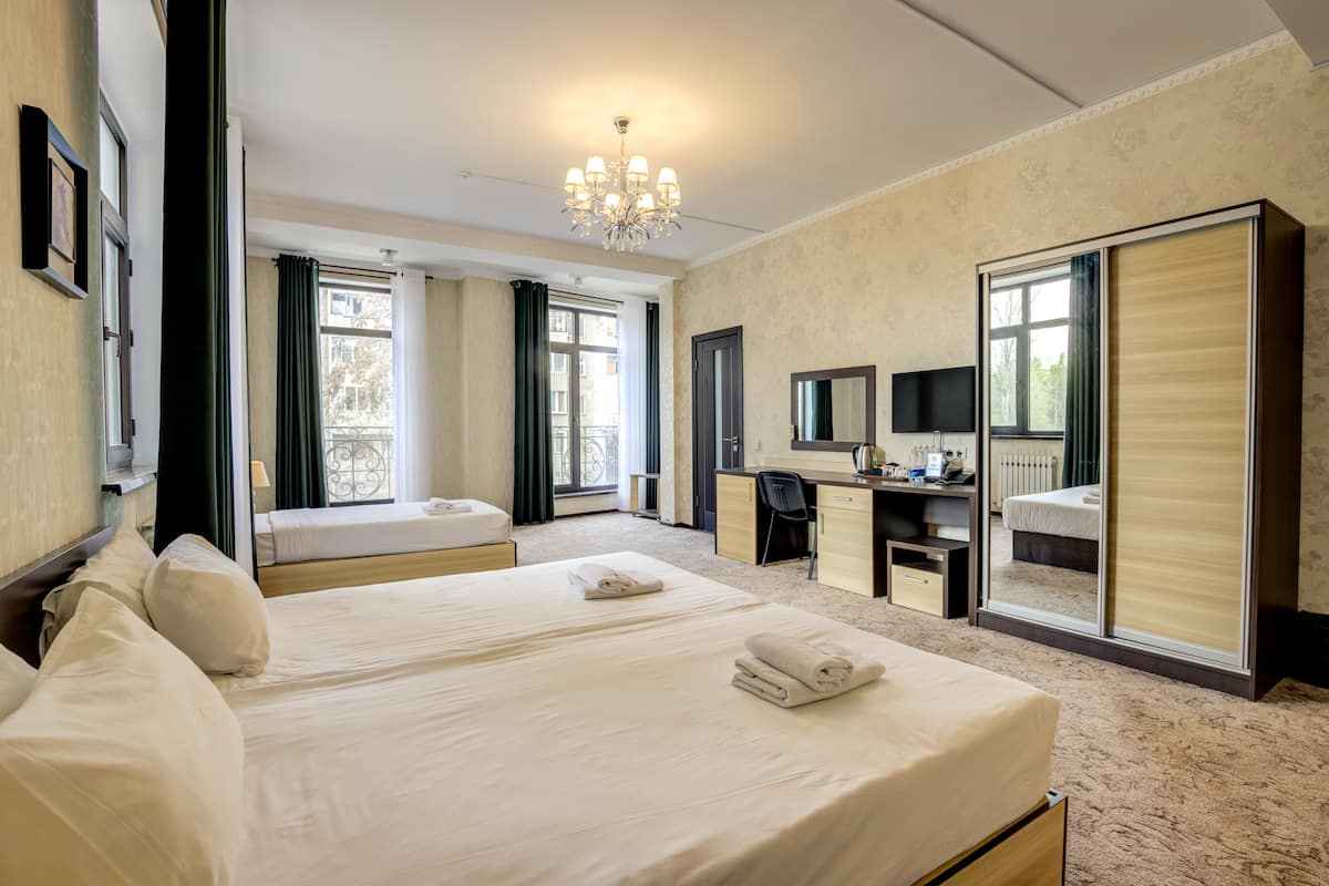 Habitación de hotel con dos camas, un escritorio, una silla, un televisor y un espejo grande.