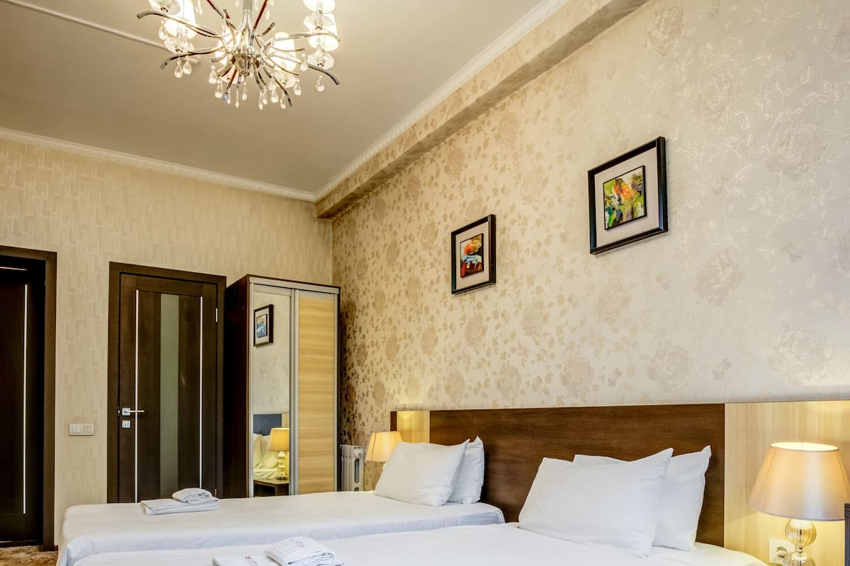 Habitación de hotel con dos camas, un candelabro, un armario y una mesita de noche con lámpara.