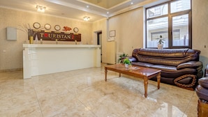 A reception area with a reception desk, a brown leather sofa, a wooden coffee table, and a large window with a view. - Hotel Touristan Bishkek (Bishkek)