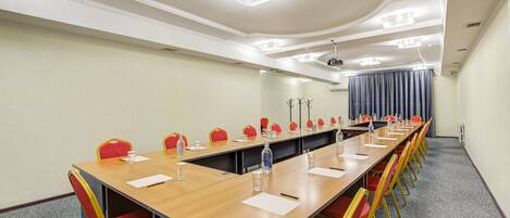 A conference room with a long table, red and yellow chairs, and ceiling lights.