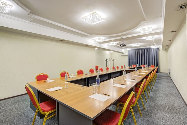 Une salle de conférence avec une longue table, des chaises rouges et jaunes, et des luminaires au plafond.