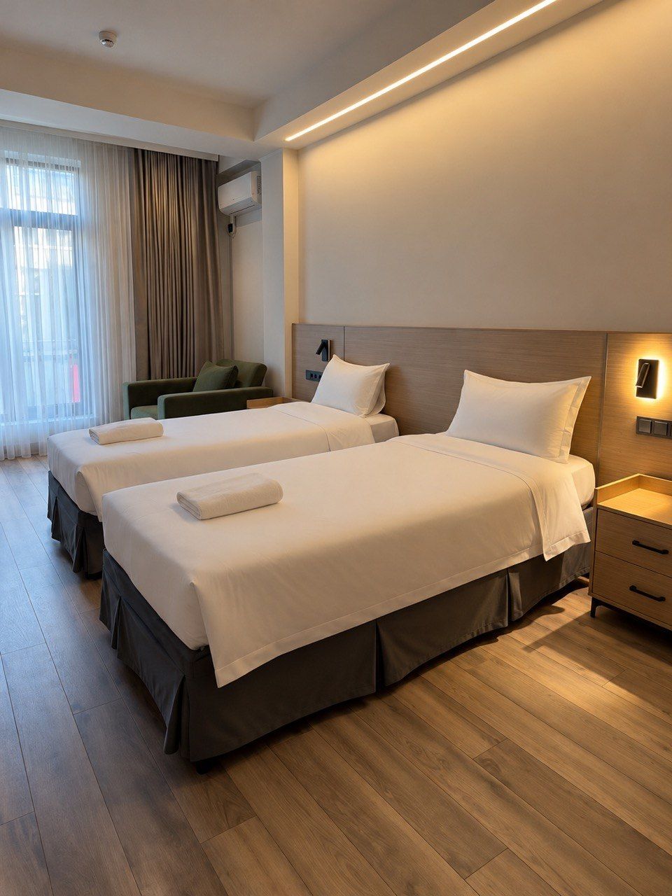 A hotel room with two beds, a desk, a chair, and a window with curtains.