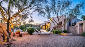 A modern outdoor patio with a hammock, seating, and a building with a staircase. - Private Desert Sanctuary with Pool, Spa, & Putting Green (Cave Creek)