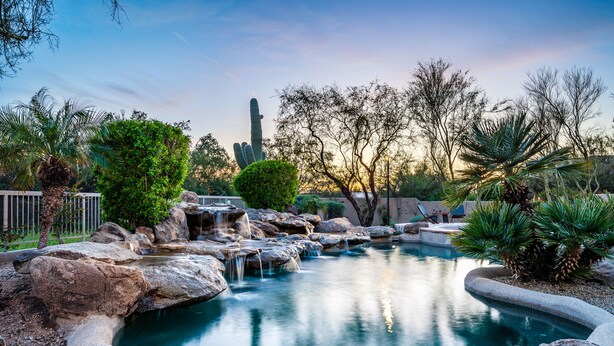 A serene outdoor pool area with natural rock formations, a small waterfall, and various trees. - Private Desert Sanctuary with Pool, Spa, & Putting Green (Cave Creek)