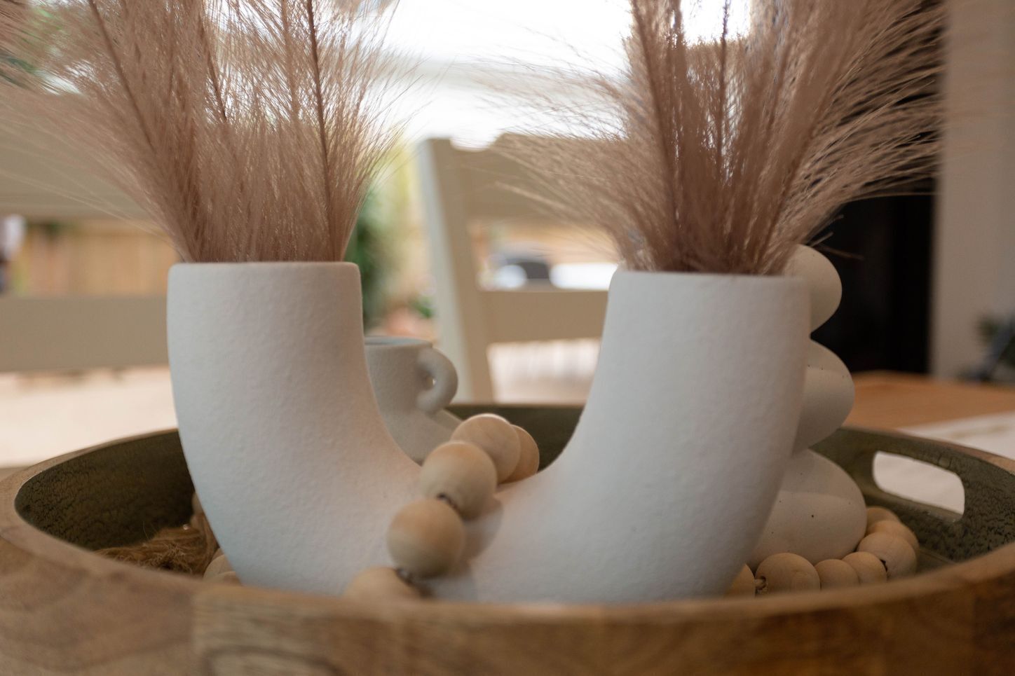 Deux vases en céramique blanche, de forme originale, sont posés sur un plateau en bois, accompagnés de petites sphères.