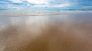 Ein Strand mit feuchtem Sand und einem bewölkten Himmel.