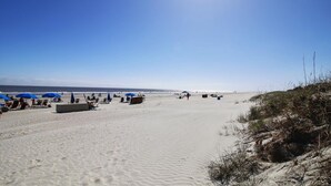 A wide sandy beach with blue umbrellas and lounge chairs, a clear sky, and a distant view of the ocean.