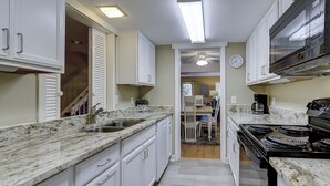 A narrow kitchen with white cabinets, a stainless steel sink, and a black stove.