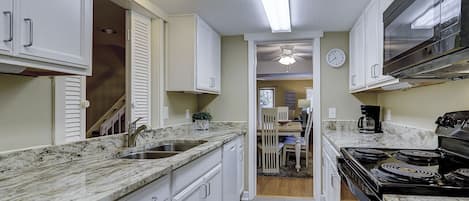 A narrow kitchen with white cabinets, a stainless steel sink, and a black stove.