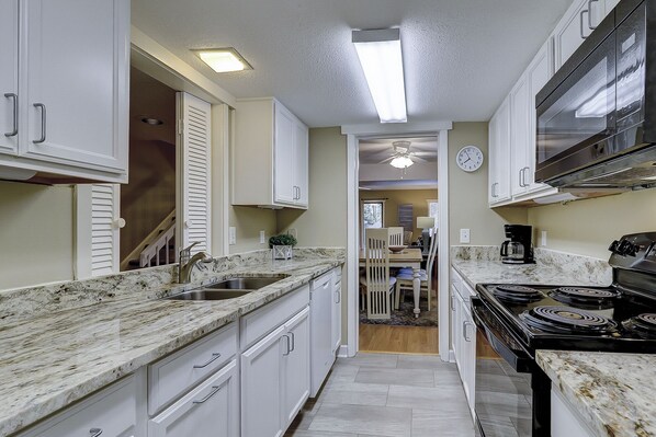 A narrow kitchen with white cabinets, a stainless steel sink, and a black stove.