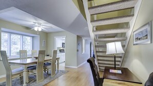 A spacious dining area with a high ceiling fan, a staircase with a cat tree, and a view of the kitchen.