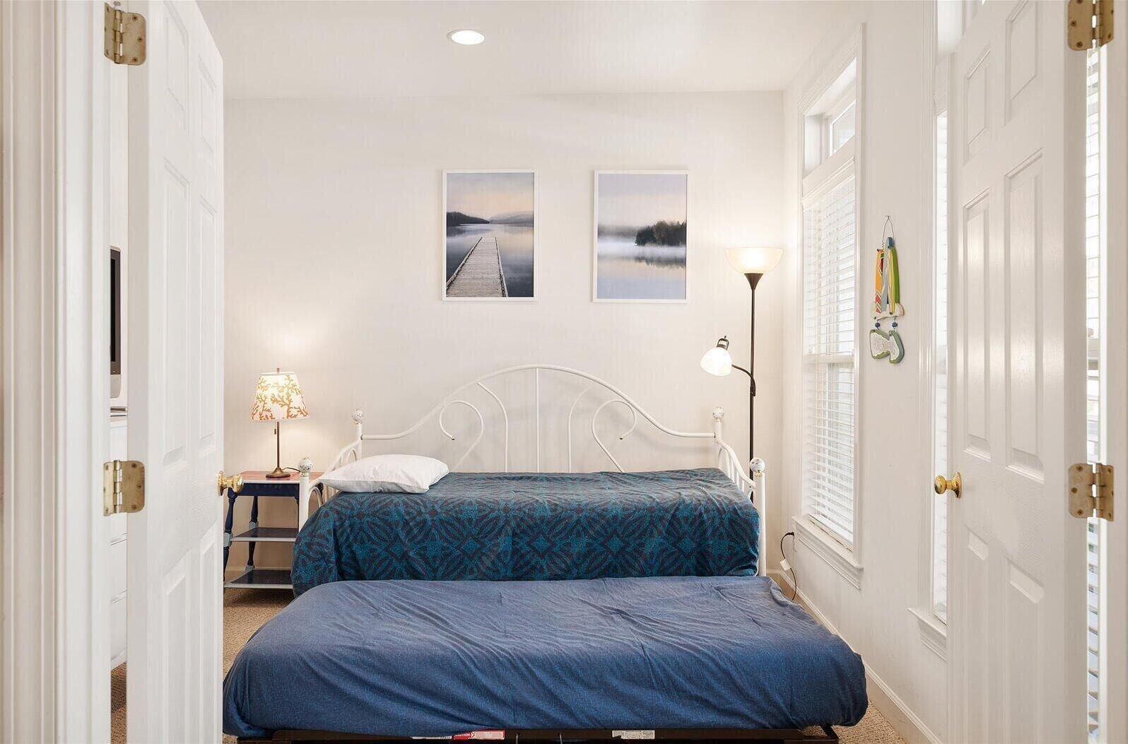 Un dormitorio con dos camas, una mesita de noche, una lámpara y dos cuadros en la pared.