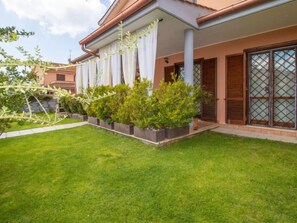 A modern house with a well-maintained lawn, a covered porch with white curtains, and a large window with a lattice design.