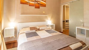 Ein Schlafzimmer mit einem großen Bett, Nachttischen, einem Schminktisch, einem Wandbild und einem Kleiderschrank mit Spiegel.