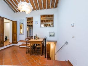 Un'area pranzo con tavolo e sedie in legno, una lampada a sospensione e una scala che conduce in un'altra stanza.