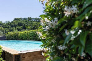 A swimming pool with a wooden deck, surrounded by lush greenery and trees.