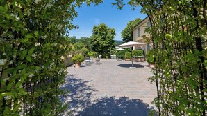 A courtyard with a paved patio, outdoor seating, and a building in the background. - Verderame – Apartment with pool (Baco)