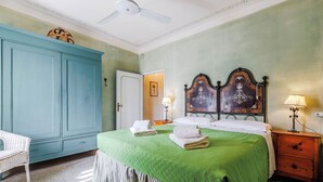 A hotel room with a bed, a wardrobe, a nightstand, a lamp, and a ceiling fan. - Verderame – Apartment with pool (Baco)