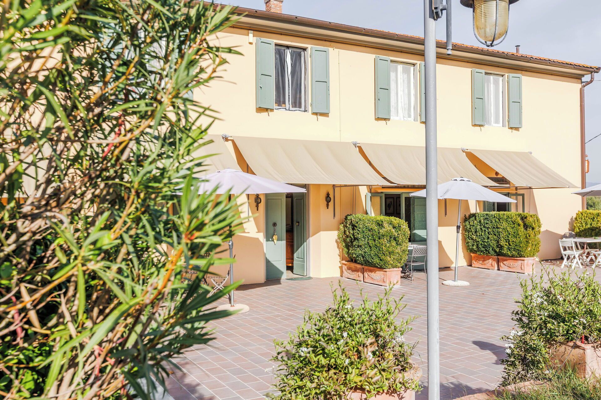Ein Gebäude mit einer gefliesten Terrasse, Sitzgelegenheiten im Freien und Blumentöpfen.