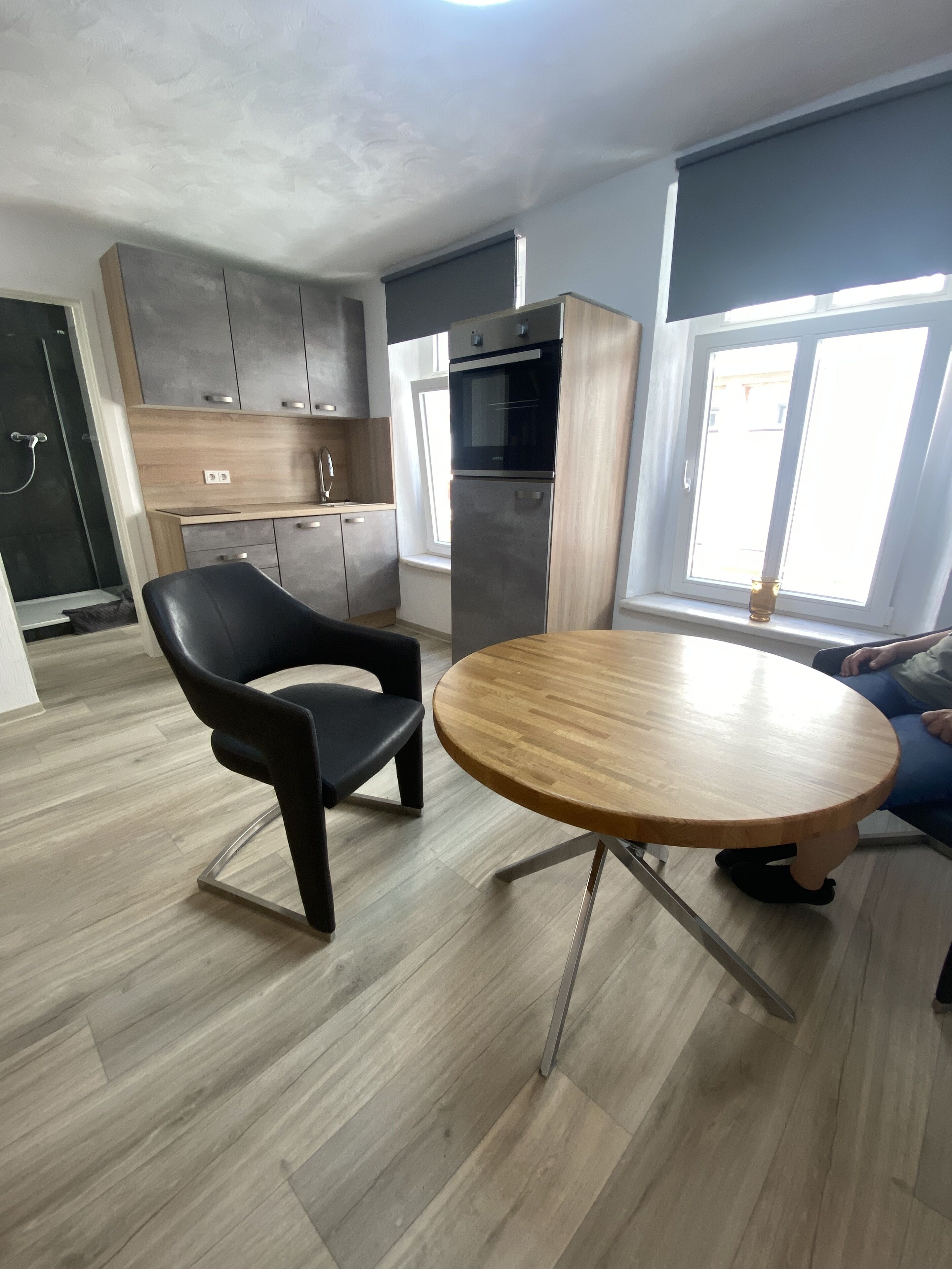 Una cocina moderna con horno empotrado y refrigerador, una mesa redonda de madera y una silla negra.
