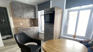 Une cuisine moderne dotée d’un four et d’un réfrigérateur encastrés, d’une table ronde en bois et d’une chaise noire.