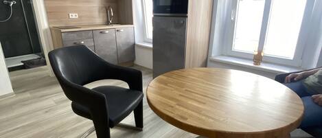 Una cocina moderna con horno empotrado y refrigerador, una mesa redonda de madera y una silla negra.